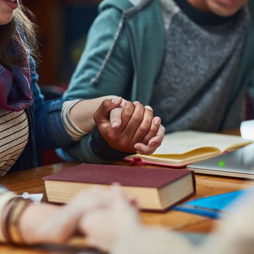 People, bible study or holding hands at table for worship, gratitude or prayer at book. Religious group, spiritual gesture or meeting in library for learning, faith or trust in christian community.